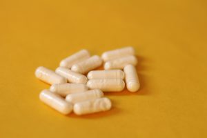 Un gruppo di capsule bianche sparse su una superficie gialla, rappresentazione di integratori o farmaci.