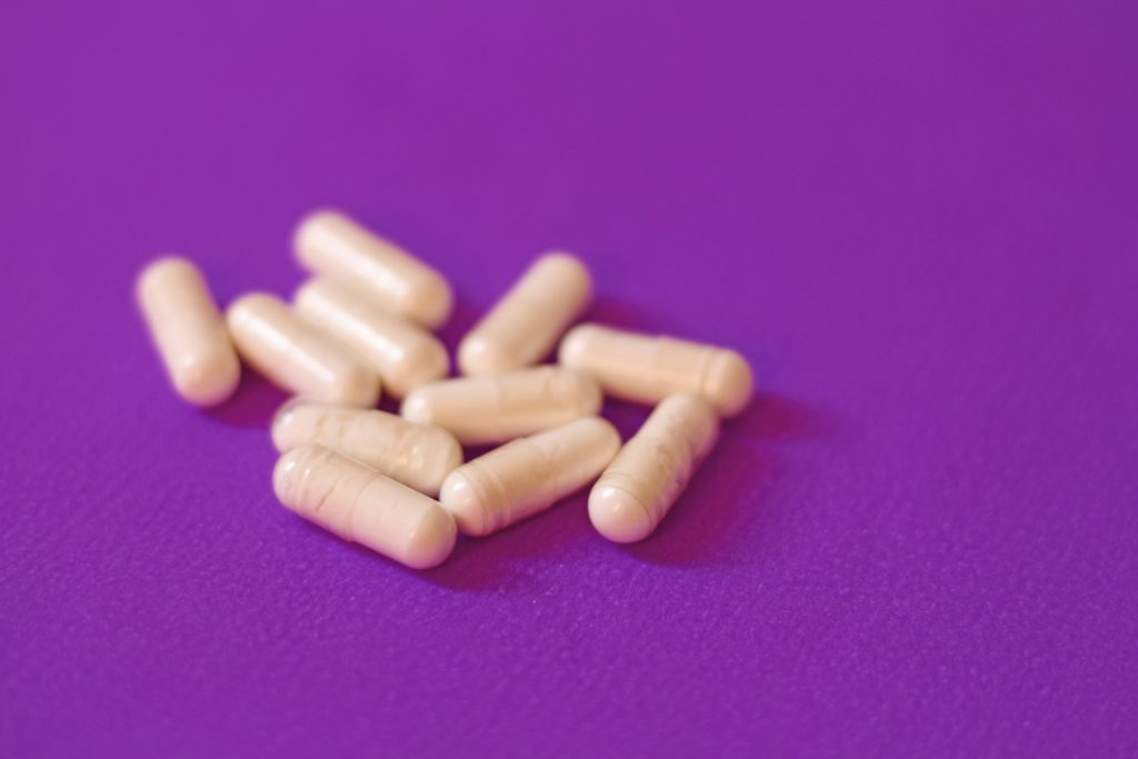 Un gruppo di capsule beige sparse su una superficie viola, rappresentazione di integratori o farmaci.