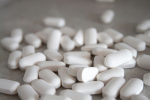 Numerose compresse bianche di forma ovale sparse su una superficie chiara, rappresentazione di farmaci o integratori.