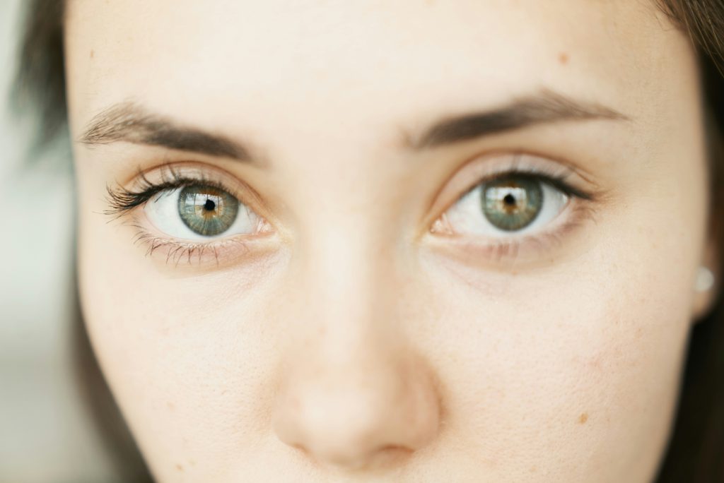 Primo piano ravvicinato del viso di una donna con occhi chiari, sopracciglia scure e incarnato naturale.