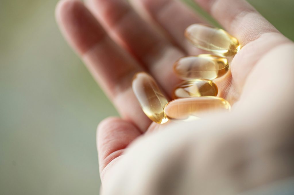 Alcune capsule trasparenti di colore dorato sono appoggiate nel palmo di una mano in primo piano