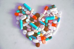 Diverse pillole e capsule colorate sono disposte a forma di cuore su uno sfondo chiaro