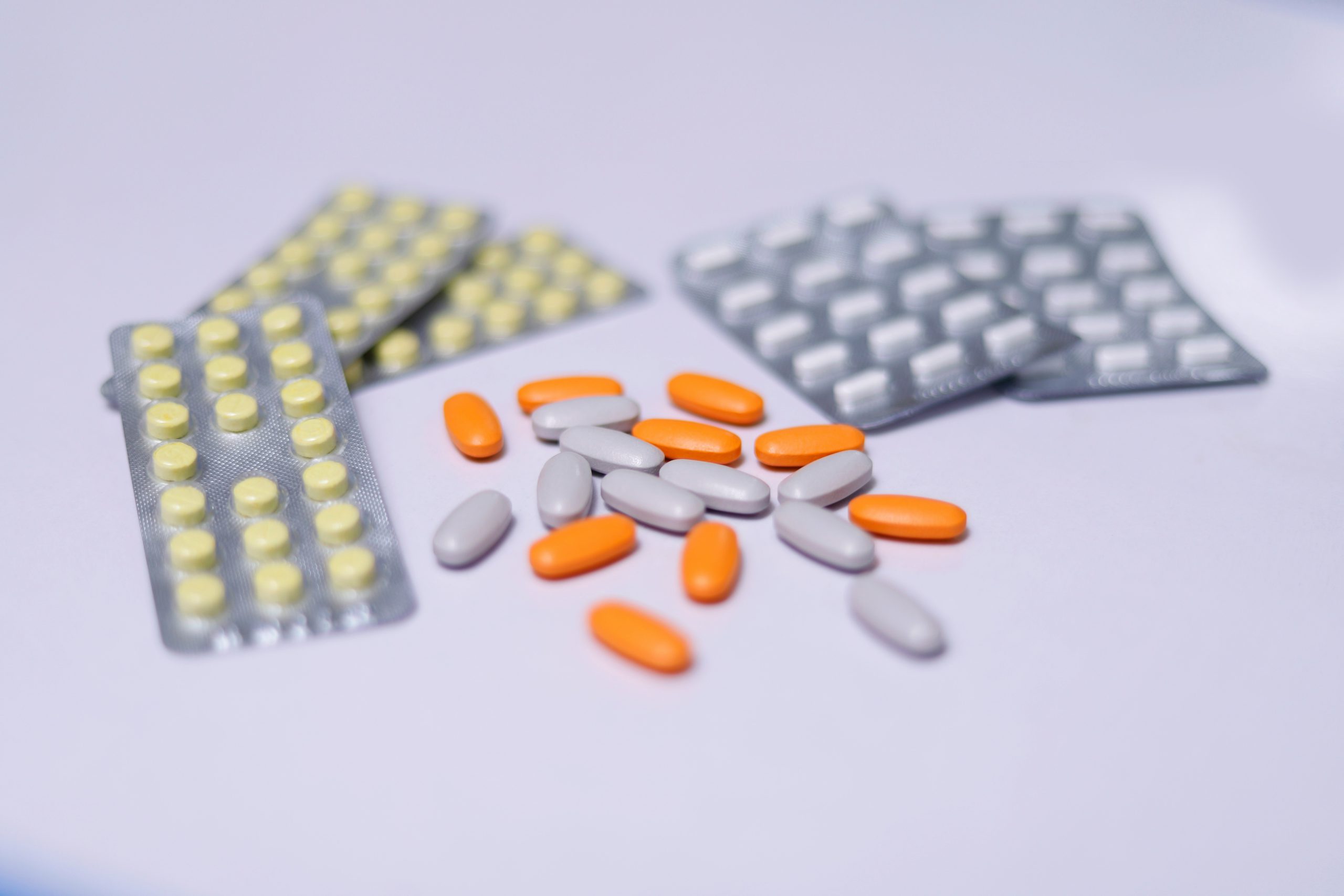 Diverse compresse arancioni e grigie sparse su una superficie chiara con blister di pillole sullo sfondo