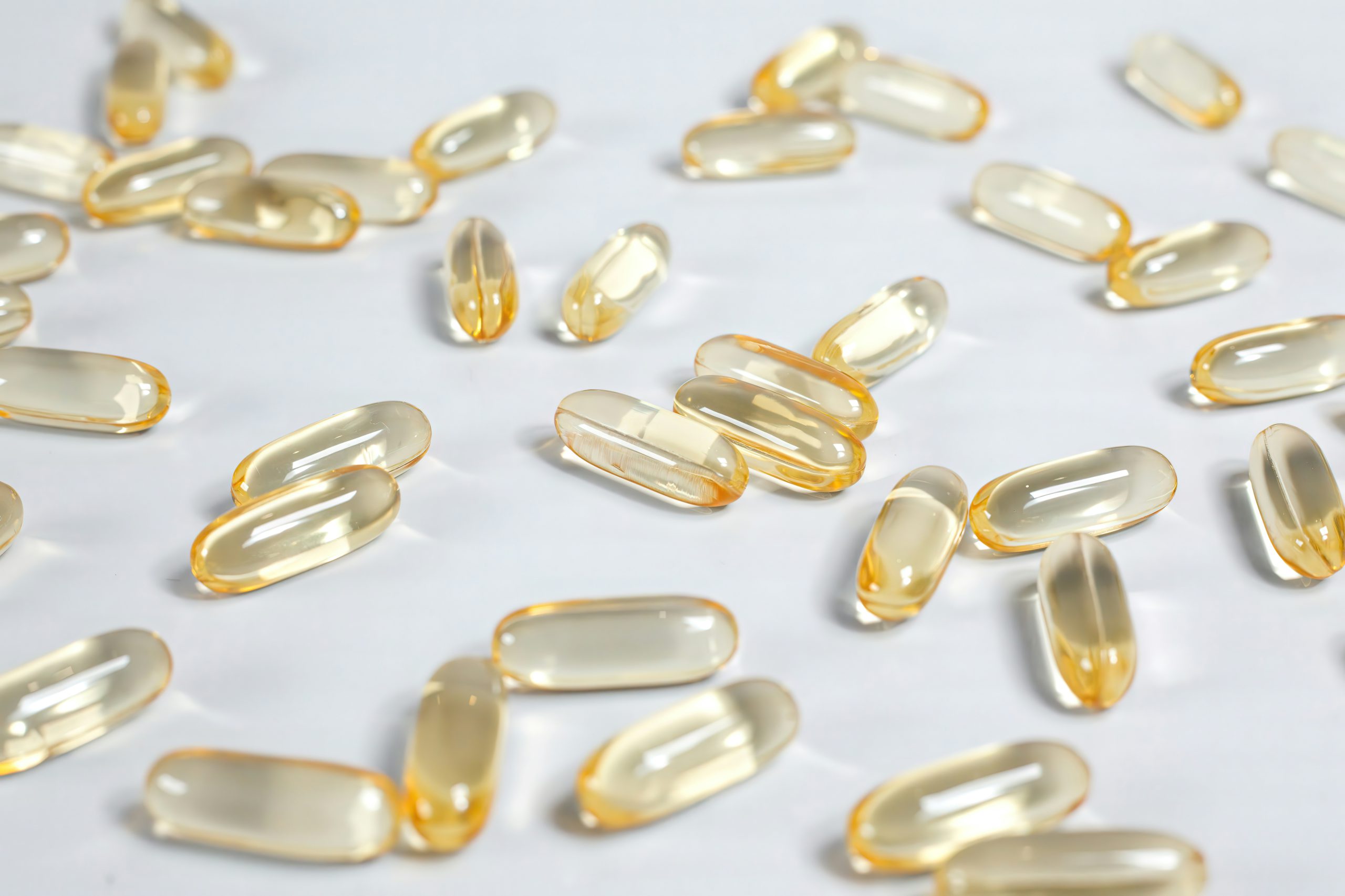 Capsule morbide trasparenti con liquido giallo, tipiche degli integratori di omega-3 o olio di pesce, sparse su una superficie bianca
