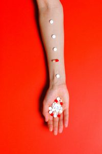 Braccio con pillole e capsule allineate su sfondo rosso acceso, che simboleggia l'assorbimento degli integratori e l'impatto del caldo estivo sui peptidi.