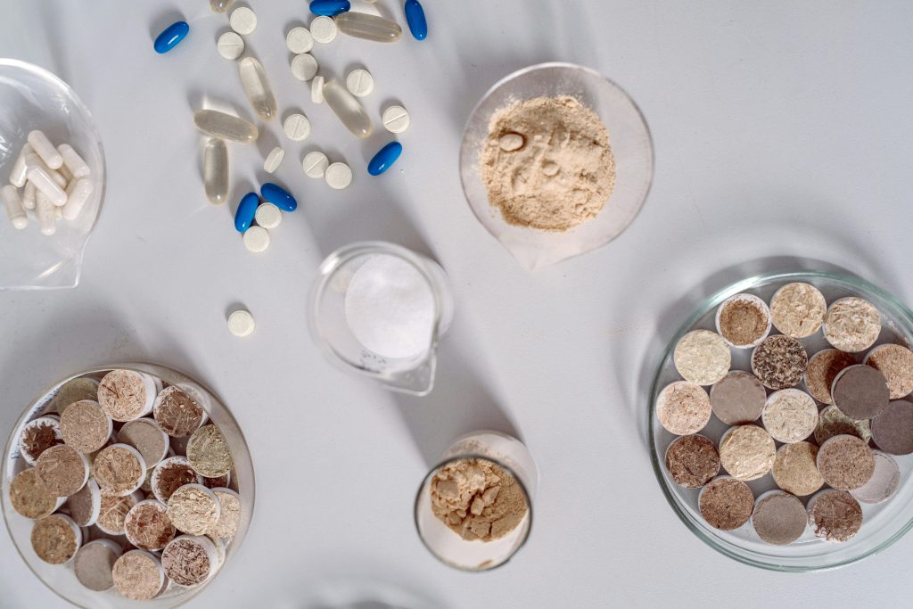 Vista dall'alto di capsule, polveri e integratori in vetreria da laboratorio, che rappresenta le formulazioni di peptidi per il supporto della tiroide.