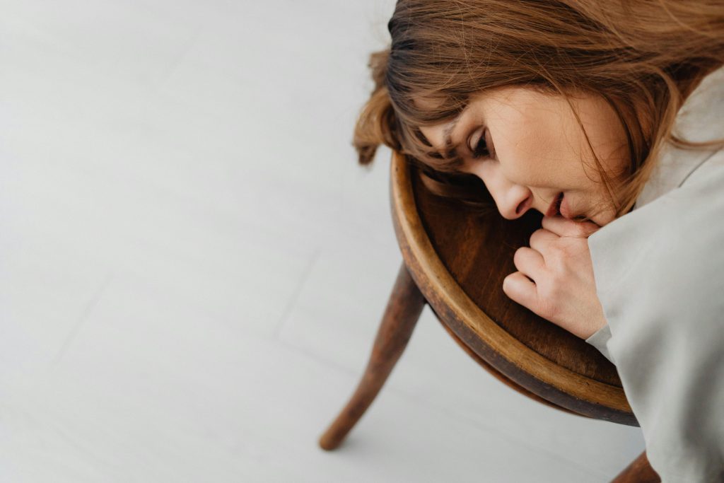 Donna visibilmente provata che appoggia la testa su una sedia di legno, a simboleggiare i crampi e i disturbi gastrointestinali durante un viaggio.